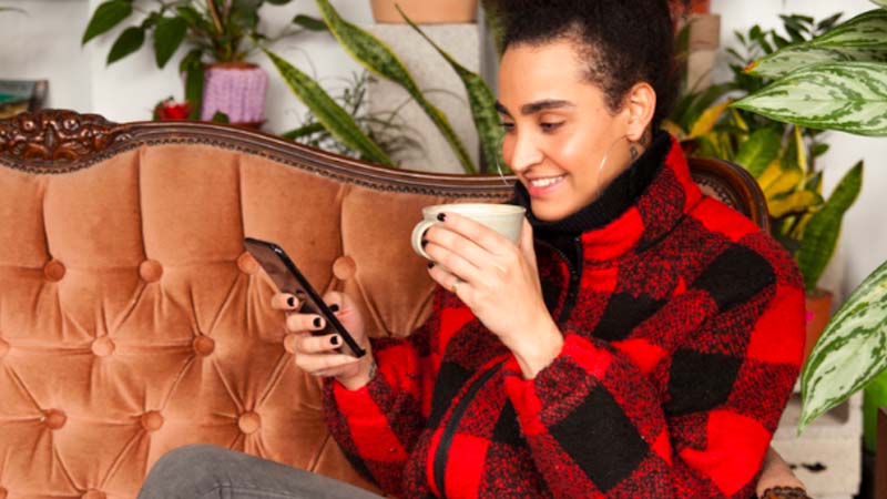 mujer tomando café mientras mira su móvil